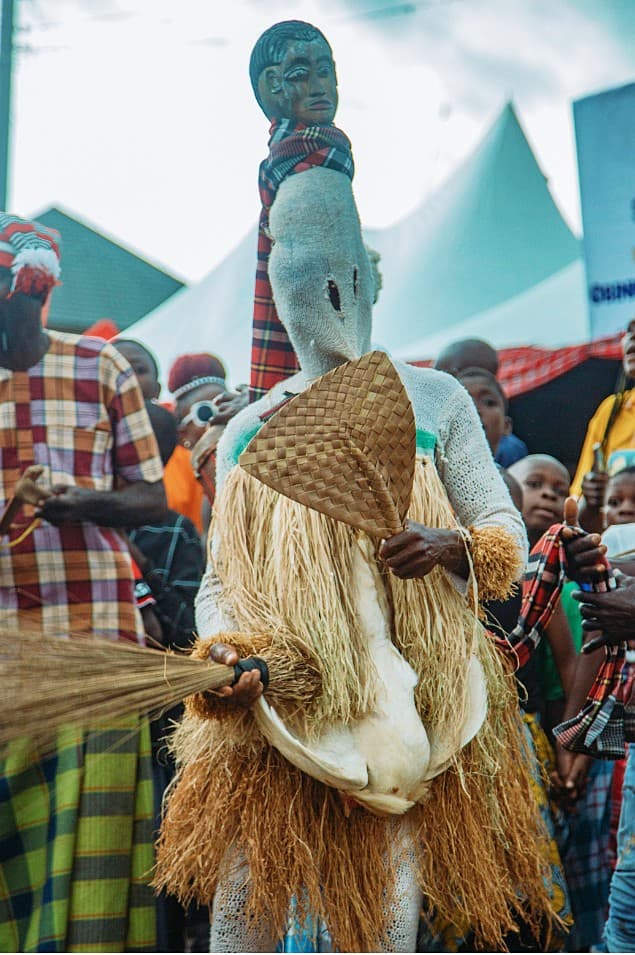 Masquerade figure in tall headpiece and raffia costume