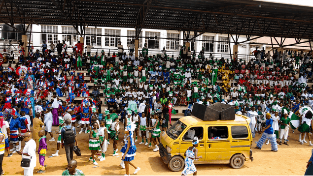 Packed grandstand and yellow danfo at the carnival grounds