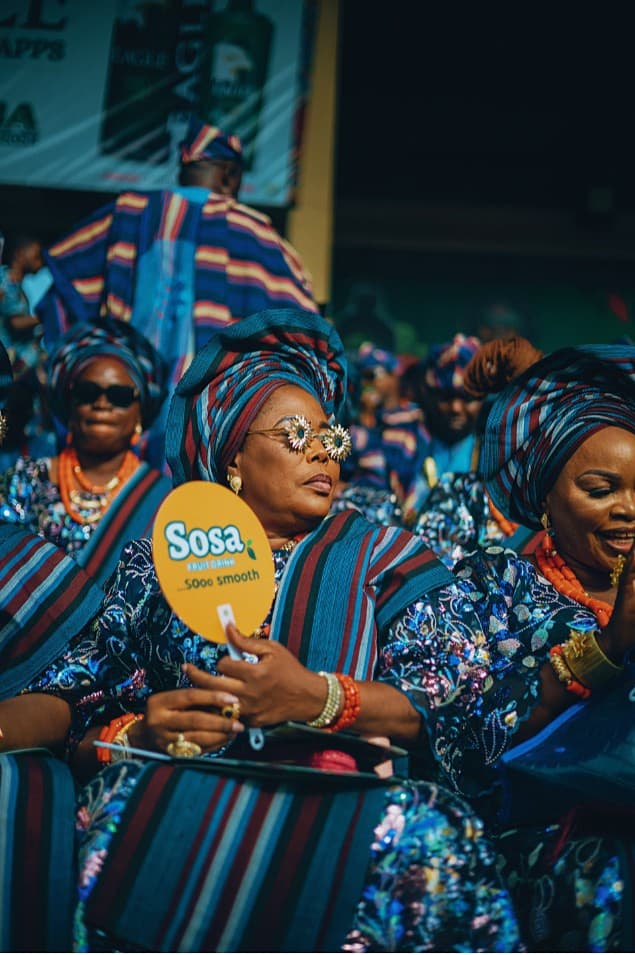 Woman in sequined aso ebi with coral beads and yellow fan