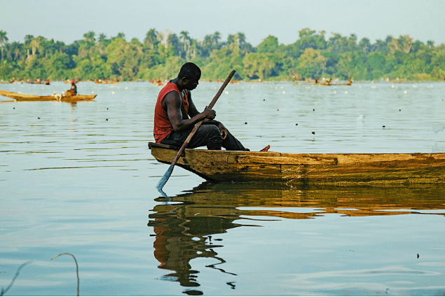 Fisherman paddling a dugout canoe at golden hour