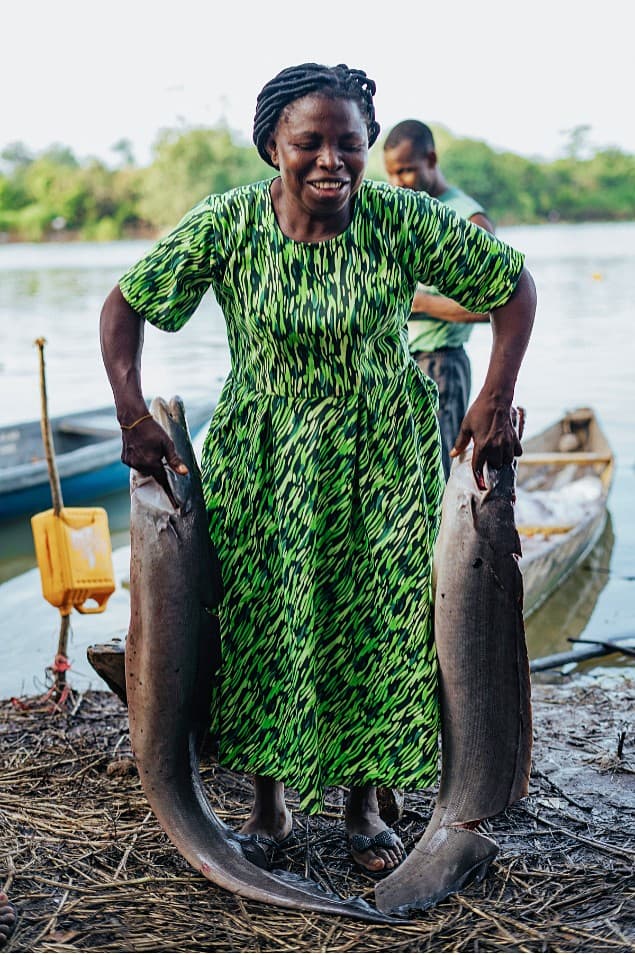 Woman celebrating with two large catfish on the riverbank