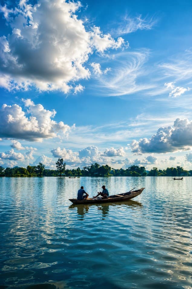 Two people in a dugout canoe on a calm river under a blue sky